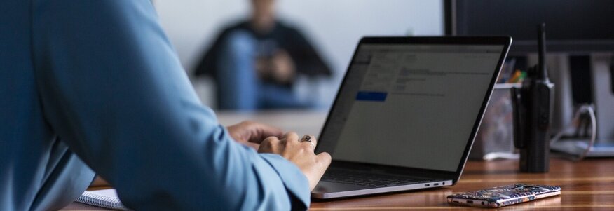 Ich sehe eine Frau mit blauer Bluse vor ihrem Laptop im Home-Office